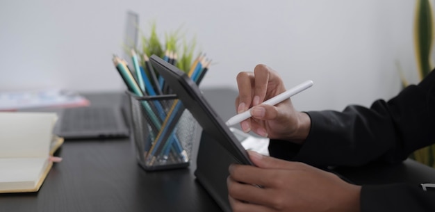 Zbliżenie dłoni kobiety z rysikiem pisania na cyfrowym notatniku, dotykając ekranu cyfrowego tabletu pracującego na komputerze przenośnym w biurze. Projektant stron internetowych przy swoim projekcie.