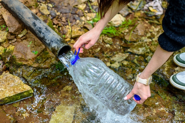 Zbliżenie dłoni mężczyzn plastikową butelką, wypełnia czystą świeżą wodą ze źródła, podziemne źródło