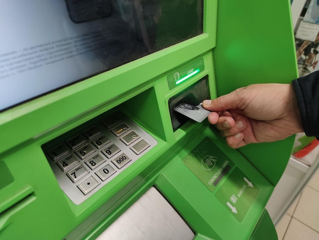 Zbliżenie dłoni mężczyzny wkładającej e-kartkę do gniazda bankomatu