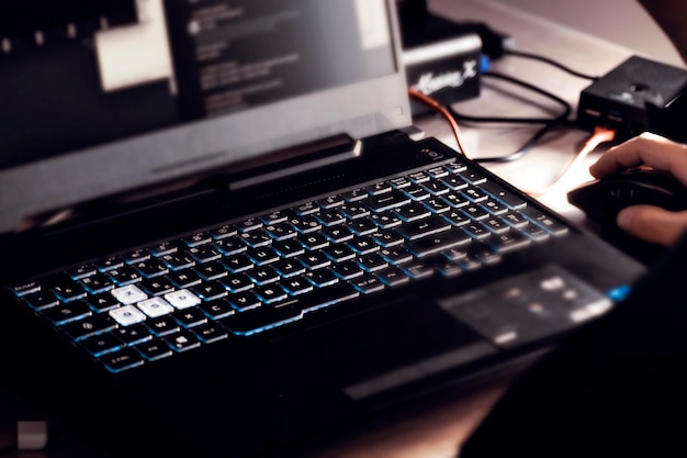 Zbliżenie dłoni mężczyzny za pomocą bezprzewodowej myszy i laptopa z podświetlaną na niebiesko klawiaturą