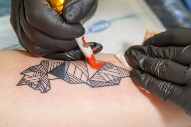 Zbliżenie dłoni mistrza tatuażu w czarnych rękawiczkach z maszyną do tatuażu