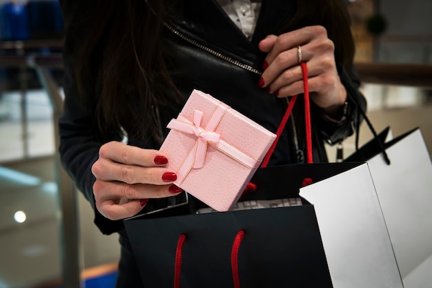 Zbliżenie dłoni młodej kobiety rasy kaukaskiej z jej paznokcie pomalowane na czerwono, trzymając czarną torbę na zakupy prezentów. Kupowanie prezentów na Nowy Rok i Święta w Galerii.