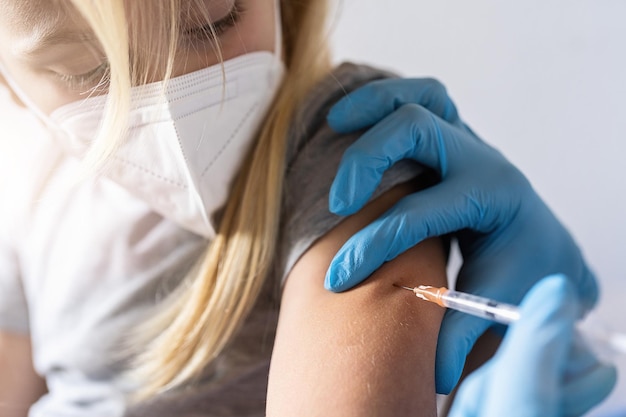 Zbliżenie dłoni pielęgniarki podającej małej blond dziewczynce pierwszą dawkę szczepionki przeciw Covid w szpitalu Zatwierdzona, zatwierdzona próba Bezpieczna dostępna Powrót do szkoły Obraz koncepcyjny szczepionki przeciw COVID 19 dla dzieci