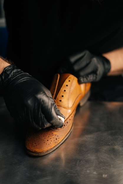 Zdjęcie zbliżenie dłoni szewca w czarnych rękawiczkach lateksowych, pocierając stare jasnobrązowe skórzane buty do późniejszej renowacji. koncepcja szewca rzemieślnika, naprawy i prace konserwatorskie w sklepie obuwniczym.