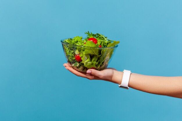 Zbliżenie dłoni trzymającej dużą szklaną miskę z zieloną sałatą ze świeżych czerwonych pomidorów i liści sałaty