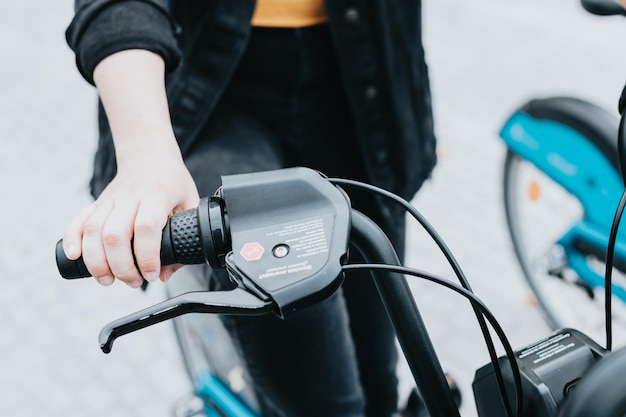 Zbliżenie dłoni trzymającej kierownicę roweru elektrycznegoMłody dorosły odblokowujący transport publiczny w mieście do zwiedzaniaRóżne sposoby poruszania się i planowania turystycznegoKorzystanie ze źródeł odnawialnych