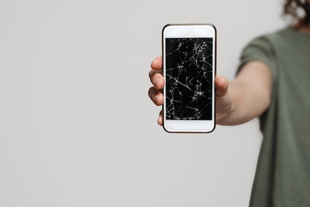 Zbliżenie dłoni trzymającej zepsuty smartfon z uszkodzoną ochroną ekranu