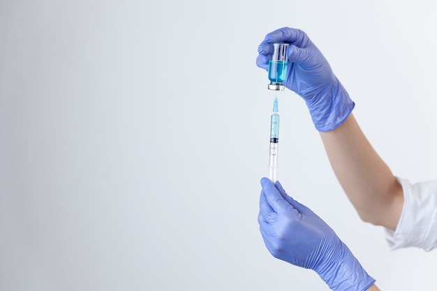Zbliżenie dłoni w fioletowych gumowych rękawiczkach trzyma i napełnia strzykawkę z butelki z niebieską szczepionką