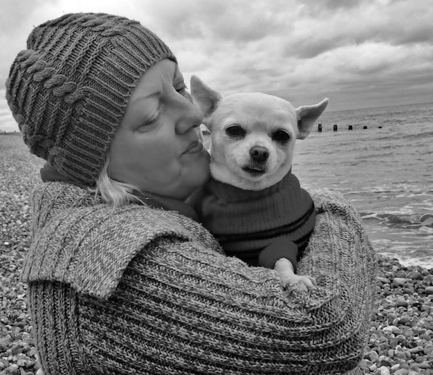 Zdjęcie zbliżenie dojrzałej kobiety trzymającej chihuahua na plaży na chmurnym niebie