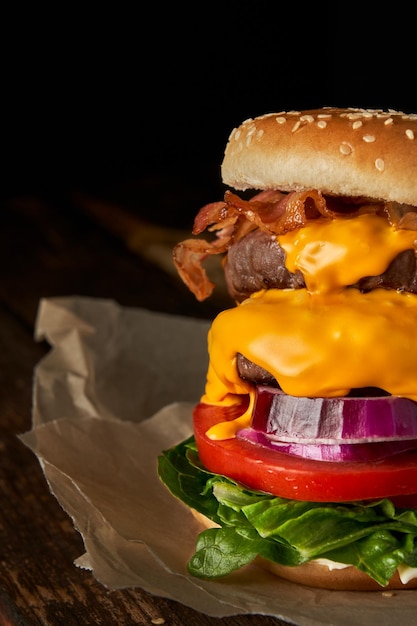 Zbliżenie domowej roboty smaczny burger z cebulową sałatą cheddar ser bekonem i pomidorem na drewnianym stole z miejsca kopii