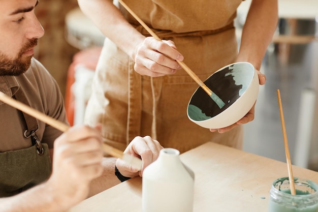 Zdjęcie zbliżenie dwóch młodych artystów dekorujących ceramikę w przestrzeni kopii warsztatu garncarskiego