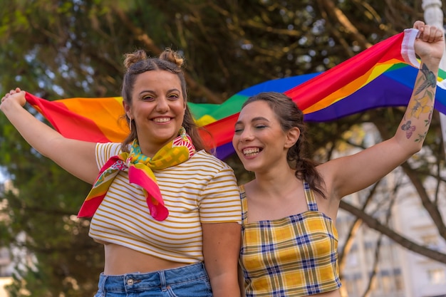 Zbliżenie dwóch młodych kobiet rasy kaukaskiej trzymających flagę dumy LGBT na zewnątrz