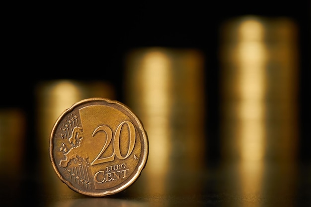 Zbliżenie dwudziestocentowej monety euro na tle stosów monet