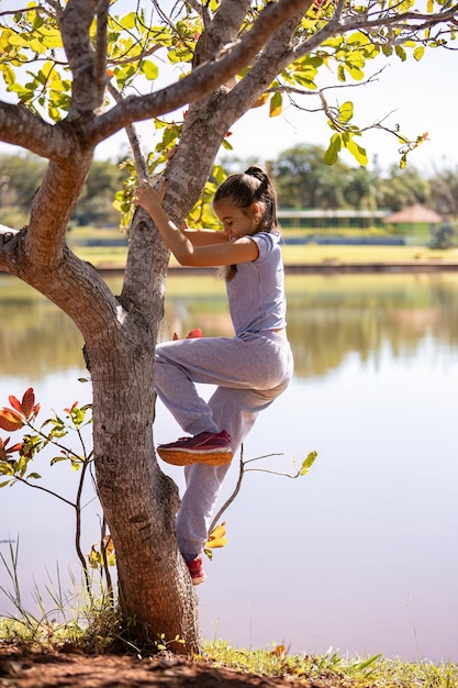 Zdjęcie zbliżenie dziecka dziewczyny w szarych ubraniach bawiącej się na drzewie w parku z selektywnym skupieniem