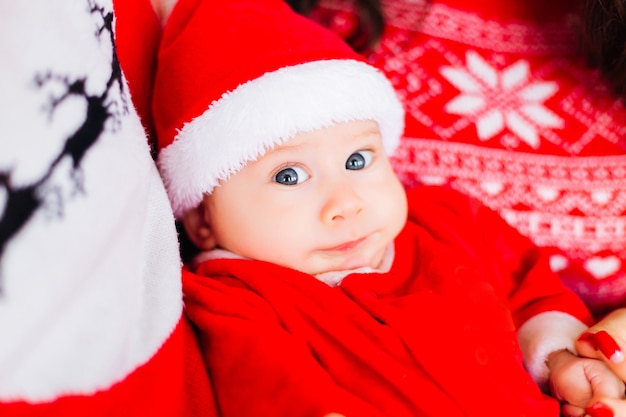 Zbliżenie dziecka o niebieskich oczach w stroju Świętego Mikołaja między rodzicami
