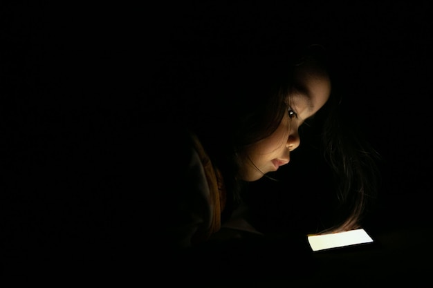 Zdjęcie zbliżenie dziecka używającego telefonu komórkowego w ciemności