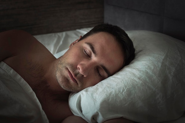 Zbliżenie głowy na poduszce podczas snu Przystojny młody mężczyzna śpi w białej pościeli w nocy