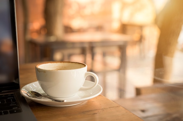 Zbliżenie: gorąca kawa latte z pianką mleczną latte art w filiżance kubek i laptop na drewniane biurko biurko w kawiarni w kawiarni, podczas koncepcji pracy biznesowej