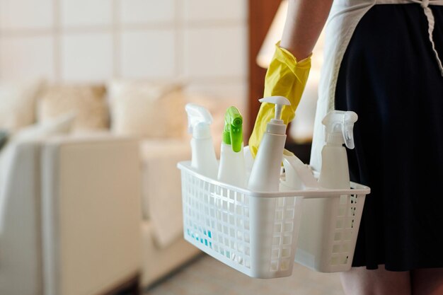 Zbliżenie gospodyni w gumowych rękawiczkach niosąc kosz z detergentami