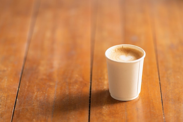 Zdjęcie zbliżenie jednorazowego papierowego kubka gorącej kawy latte z pianką mleczną w kształcie serca