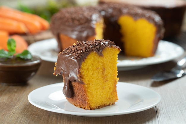Zbliżenie kawałek brazylijskiego ciasta marchewkowego z polewą czekoladową na drewnianym stole z marchewką w tle
