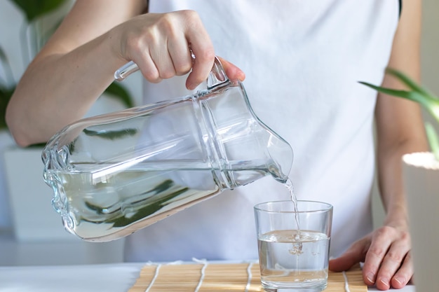 Zbliżenie kobiece dłonie wlewając wodę pitną do szklanki porannych rytuałów dla zdrowia