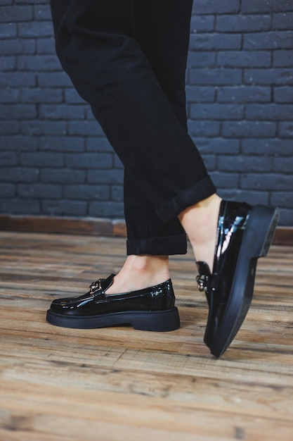 Zbliżenie kobiece nogi w czarnych spodniach i skórzane czarne buty Damskie buty z lakierowanej skóry z metalową klamrą Nowa wiosennoletnia kolekcja damskich skórzanych butów 2022