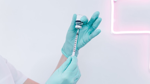 Zbliżenie kobiecej ręki lekarza z ochronnymi gumowymi rękawiczkami trzymającymi strzykawkę ze szczepionką
