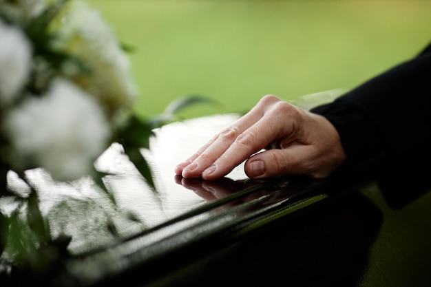 Zdjęcie zbliżenie kobiecej ręki na trumnie, żegnającej się na ceremonii pogrzebowej na świeżym powietrzu