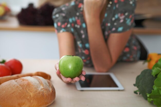 Zbliżenie kobiecej ręki trzymającej zielone jabłko w kuchniach wnętrzach Wiele warzyw i innych posiłków przy szklanym stole jest gotowych do ugotowania wkrótce