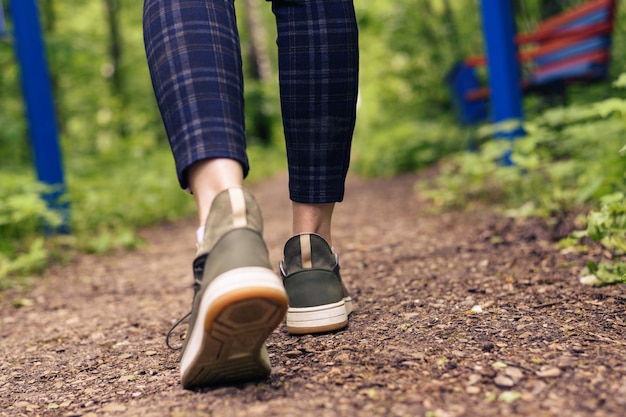 Zbliżenie kobiet nogi w zielone trampki i spodnie w klatce iść na leśnej drodze. HLS, idź na świeżym powietrzu