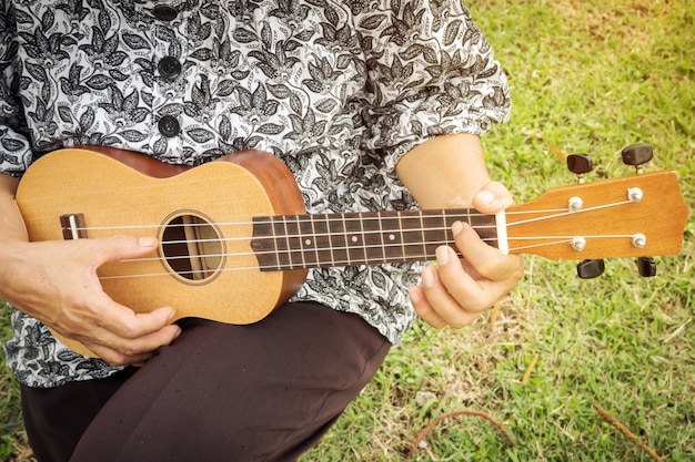 Zbliżenie kobieta bawić się ukulele. Siedząc na trawie.