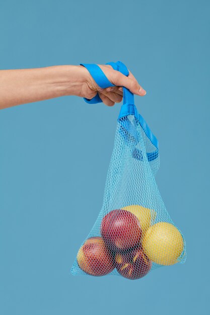 Zbliżenie: kobieta ręka trzyma torbę z owocami na białym tle na niebieskim tle