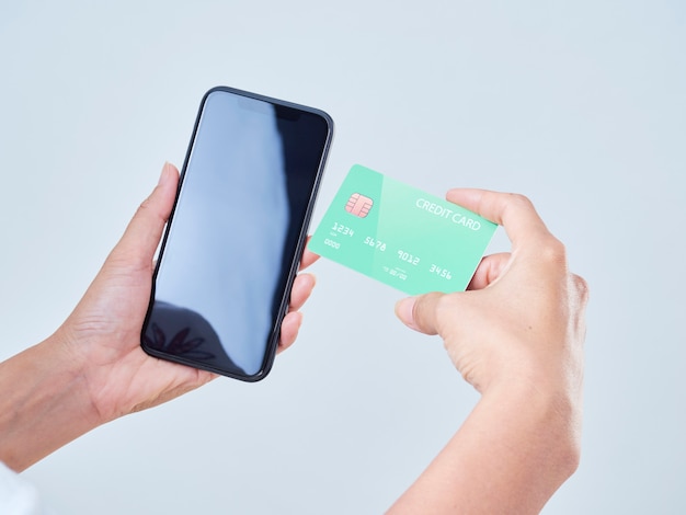 Zbliżenie: kobieta trzyma telefon komórkowy, pusty ekran i kredytową kartę bankową na szarym tle