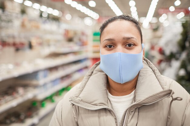 Zbliżenie: kobieta ubrana w maskę ochronną patrząc na kamery, stojąc w sklepie