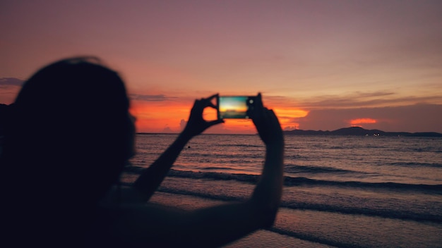 Zbliżenie kobiety młody turysta fotografuje widok na ocean z smartphone podczas zachodu słońca na plaży