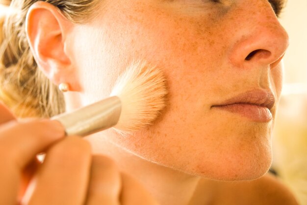 Zdjęcie zbliżenie kobiety nakładającej makijaż szczotką