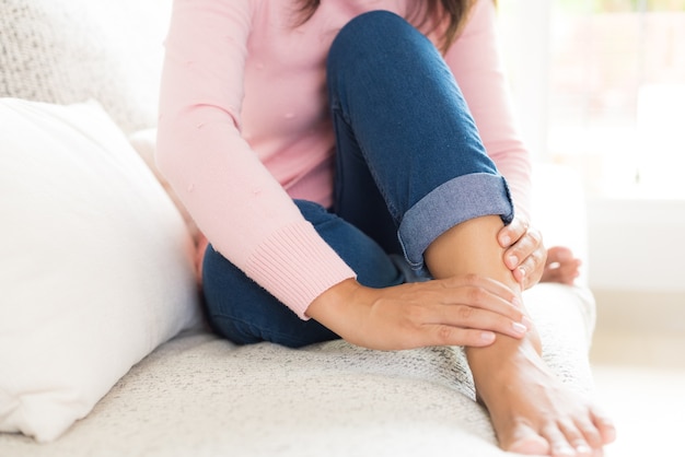 Zbliżenie kobiety obsiadanie na kanapie trzyma jej obrażenie stopy, czuje ból.