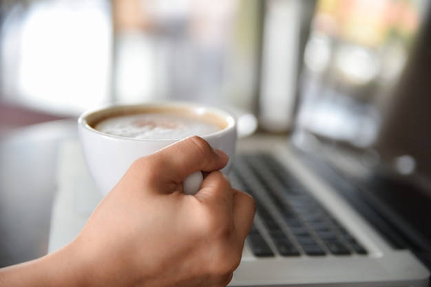 Zbliżenie kobiety ręce trzymając kubek kawy cappuccino podczas pracy w biurze.