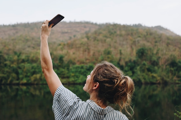 Zbliżenie kobiety ręka podnosi jej smartphone w górę brać fotografię natury podróż i turystyki concep