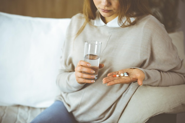 Zbliżenie kobiety trzymającej tabletki czas na przyjmowanie leków, lekarstwo na ból głowy, leki przeciwbólowe na wysokie ciśnienie krwi w domu. Koncepcja pozostania w domu podczas pandemii koronawirusa.