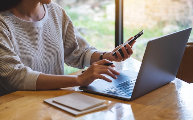 Zbliżenie kobiety trzymającej telefon komórkowy i komputer przenośny w biurze i korzystających z nich