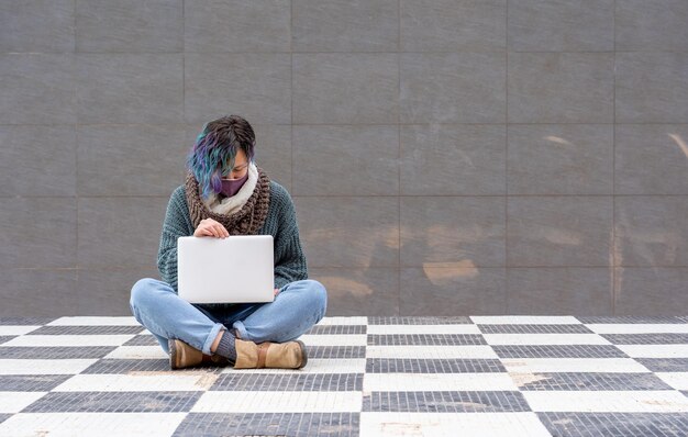 Zbliżenie kobiety w masce na twarz siedzącej na podłodze szachowej z laptopem