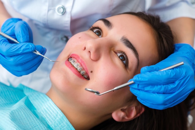Zbliżenie kobiety z nawiasami podczas leczenia aparatami ortodontycznymi w klinice Ortodonta za pomocą lusterka dentystycznego i kleszczyków podczas zakładania aparatów ortodontycznych na zęby pacjenta Koncepcja stomatologii