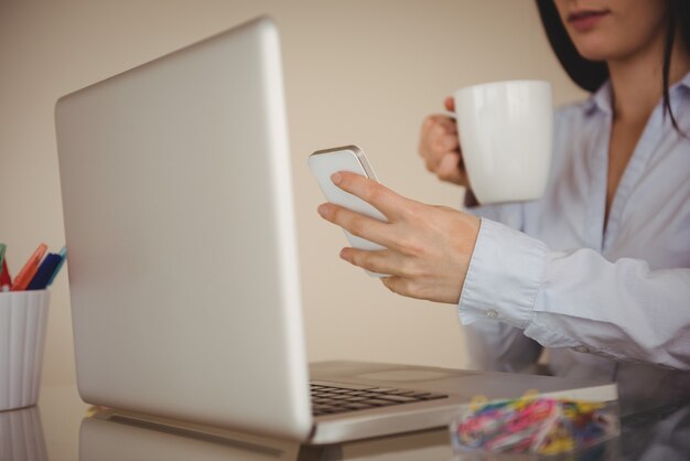 Zbliżenie Kobiety Za Pomocą Inteligentnego Telefonu Siedząc Przy Laptopie