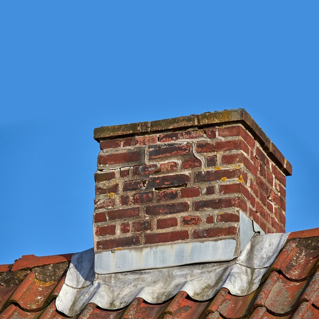 Zbliżenie komina z czerwonej cegły na dachu azbestowym na tle błękitnego nieba Projekt architektury budynku domu do oddymiania z kominka lub pieca Gazy spalinowe do izolacji domu