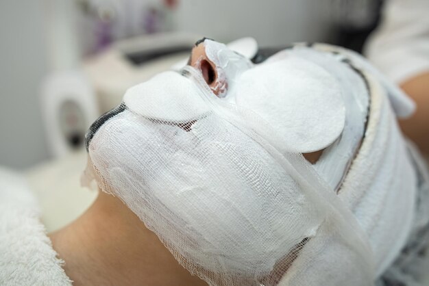 Zdjęcie zbliżenie kosmetologa stosującego białą kosmetyczną maskę na twarz dla swojej pacjentki w salonie spa