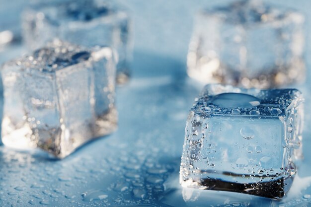 Zdjęcie zbliżenie kostek lodu z kroplami stopionej wody rozrzuconymi na niebieskim stole. makro. orzeźwiający lód do drinków i koktajli w gorący, parny dzień.