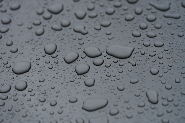 Zbliżenie kropli deszczu na czarnym masce samochodu w tle