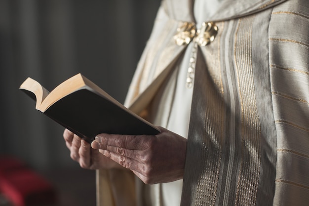 Zbliżenie: ksiądz trzymający Biblię i czytający modlitwy podczas ceremonii w kościele